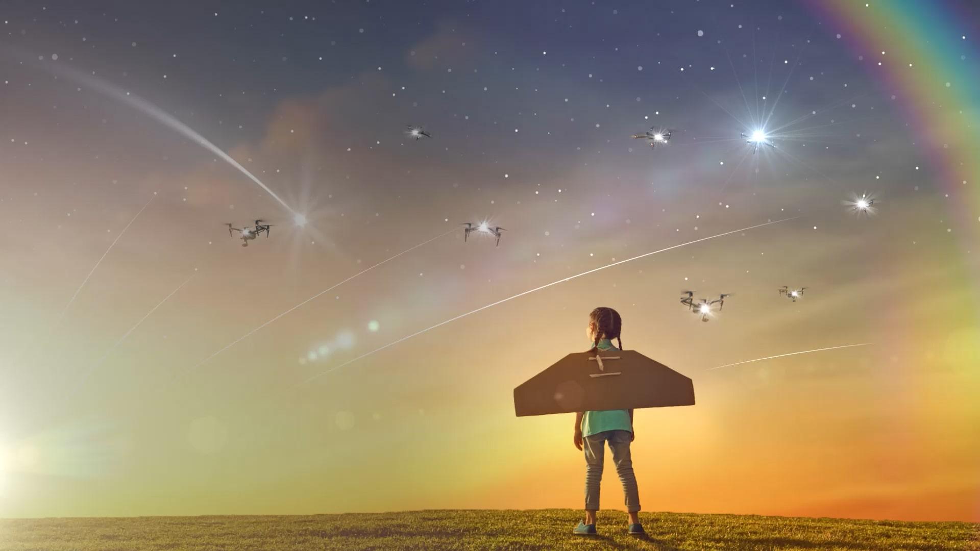 Several drones flying over the starry sky and a costumed child with wings on his back looking at the sky.