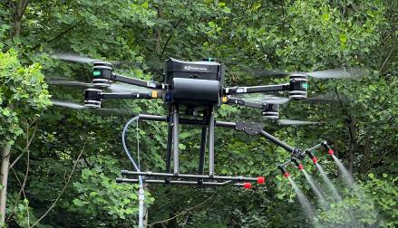 Drone Spraying: Drone cleaning surface with a low-pressure sprayer near trees.