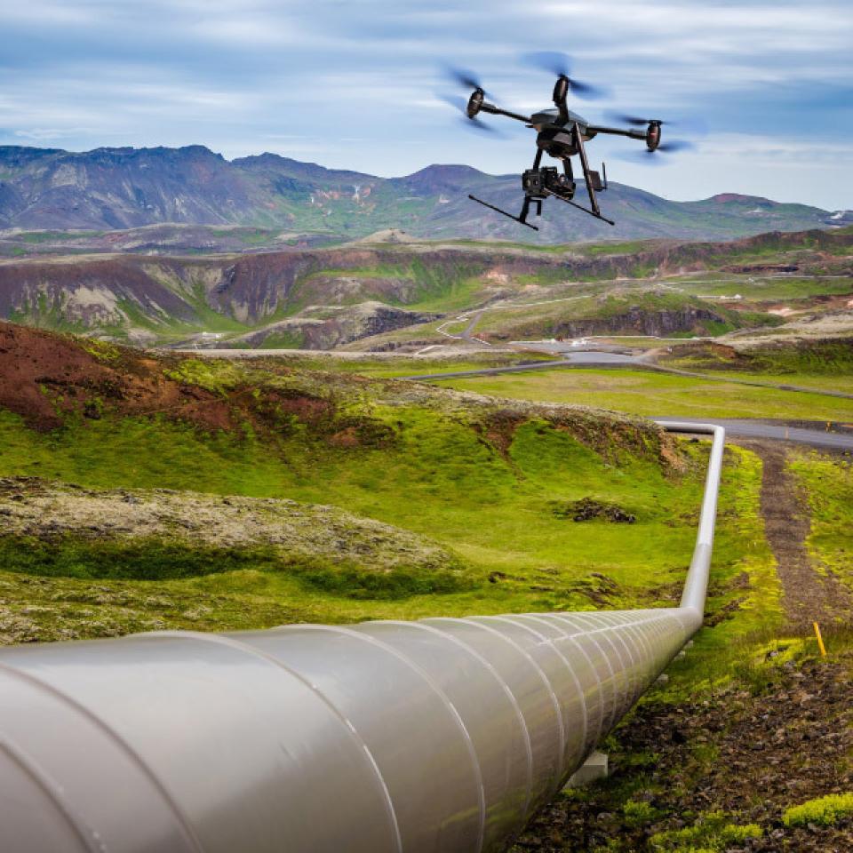 A drone flying over an oil pipeline in a green landscape.